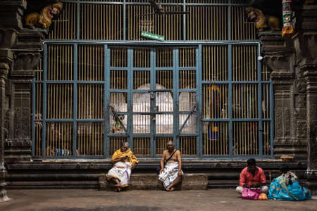 Kumbakonam, Tamil Nadu, India - February 2020: Priests and pilgrims sitting in front of large grilled doors in a dark hall of the ancient Hindu temple of Swamimalai.のeditorial素材