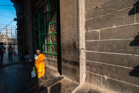 Chidambaram, Tamil Nadu. India - February 2020: An elderly Indian woman in a bright orange sari walking past the stone walls of the ancient Nataraja temple in Chidambaram.のeditorial素材