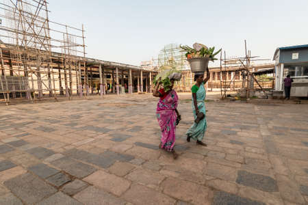 Chidambaram, Tamil Nadu. India - February 2020: Indian women laborers walking carrying baskets of vegetables on their heads inside the ancient Nataraja temple complex in Chidambaram.のeditorial素材