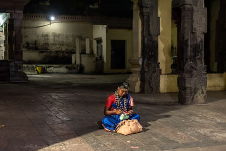 Kumbakonam, Tamil Nadu, India - February 2020: An elderly Indian woman wearing a large necklace of beads reading religious texts on the floor of a dark hall of an ancient temple.のeditorial素材