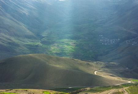 Himalayan landscape of sunlight falling on a road winding through a hill and green fields beyond in...