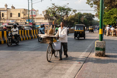 Mysuru, Karnataka, India - January 2019: A street vendor walking with his bicycle on a busy road in...