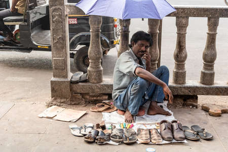 Mysuru, Karnataka, India - January 2019: A street cobbler sitting under an umbrella on the pavement in the city of Mysore.のeditorial素材