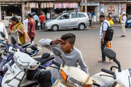 Mysuru, Karnataka, India - January 2019: A young Indian boy checking his eyes in the mirror of a bike on the streets of the city.のeditorial素材