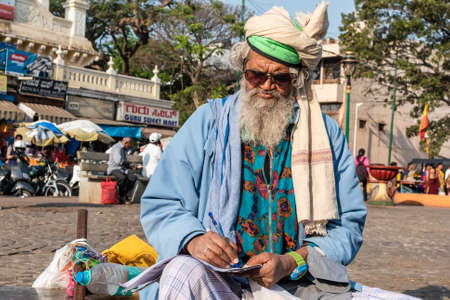 Mysuru, Karnataka, India - January 2019: Portrait of an elderly Indian man wearing sunglasses sitting alone outside and writing.のeditorial素材