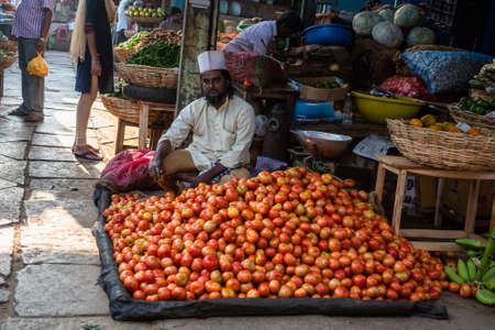 Mysore, Karnataka, India - January 2019: An Indian street vendor selling tomatoes at his roadside stall in a busy vegetable market in the city of Mysuru.のeditorial素材