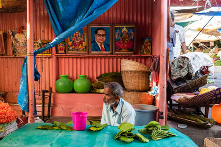 Mysore, Karnataka, India - January 2019: An elderly Indian man selling betel leaves at his street side shack with a picture of Babasaheb Ambedkar on his wall.のeditorial素材