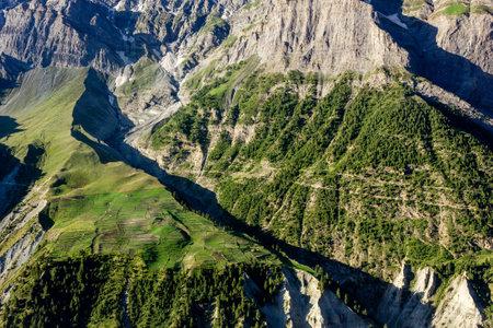 Landscape of green fields and forests on the steep slopes of a Himalayan mountain in the town of Keylong in Lahaul in Himachal Pradesh, India.の写真素材