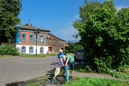 SUZDAL, RUSSIA - AUGUST 19, 2017. Three boys playing with a public water tap on the street near the old wooden residential house. Suzdal, Vladimir region, Russiaのeditorial素材