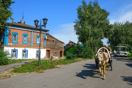 SUZDAL, RUSSIA - AUGUST 19, 2017. A man driving a horse drawn carriage on the streets of Suzdal in front of the old wooden house on a summer afternoon. Suzdal, Golden Ring, Russia.のeditorial素材