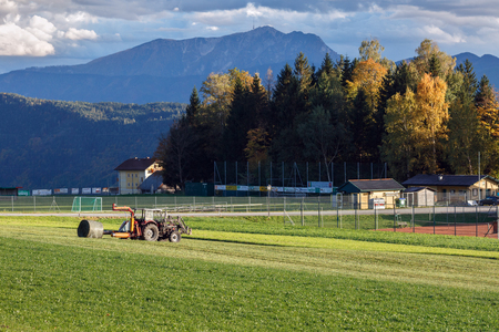 OBERMILLSTATT/ AUSTRIA - OCTOBER 8, 2017. Tractor hay bale wrapper, picking up and applying plastic cling wrap to a round bale. Village Obermillstatt, Gurktal Alps, Carinthia, Austriaのeditorial素材