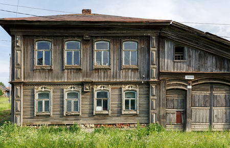 Village street in summer. Dilapidated wooden residential house with carved facade. Village of Visim, Sverdlovsk region, Urals, Russiaのeditorial素材