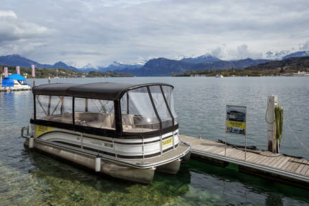LUZERN, SWITZERLAND - APRIL 16, 2018. Empty taxi boat moored to a wooden pier on lake Lucerne. View of the snow-capped Alps. Town of Luzern, canton of Luzern, Switzerland, Europe.のeditorial素材