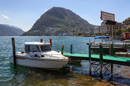 LUGANO, SWITZERLAND - APRIL 17, 2018. Empty taxi boat moored to a pier on lake Lugano on a spring sunny day. View of the San Salvatore mountain. Canton of Ticino, Switzerland, Europe.のeditorial素材
