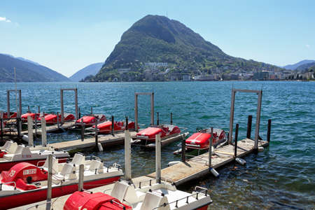 LUGANO, SWITZERLAND - APRIL 17, 2018. City of Lugano at the lake Lugano, surrounded by Alps. View of the water bikes at the pier. Lugano, canton of Ticino, Switzerland, Europe.のeditorial素材