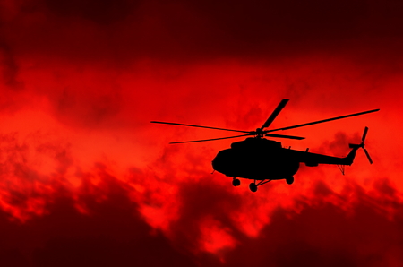 transport helicopter silhouetted against a fiery red sky with cloudsの写真素材