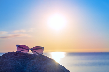 sunglasses on a stone near the sea shore. sunrise blue sky horizon. toningの写真素材
