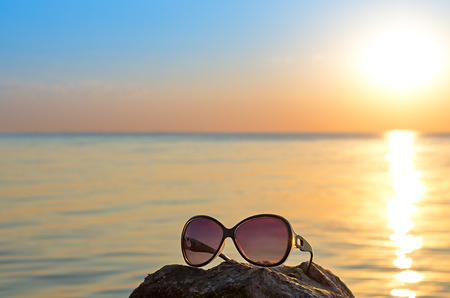 women's sunglasses on the stone, against the background of the sea and the sunの写真素材