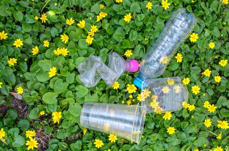 discarded plastic bottles and packaging in the grass with yellow flowersの写真素材