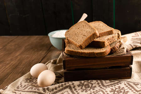 Slices of bread in box and bowl of flour with eggs on tablecloth