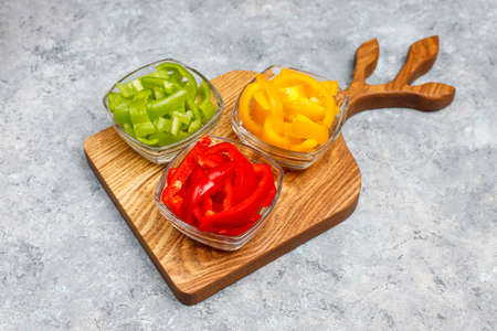 Cutting board with slices of colorful bell peppers on light background. Sliced sweet peppers in different colors, vegetable salad ingredient, cooking healthy food, top viewの写真素材