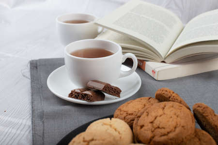 Book, cup of tea and chocolate on the tableの写真素材