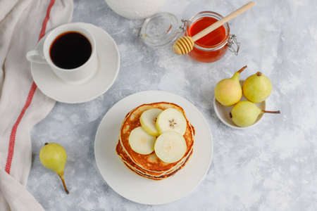 Homemade breakfast: american style pancakes served with pears and honey with a cup of tea on concrete background. Top view and copy spaceの写真素材