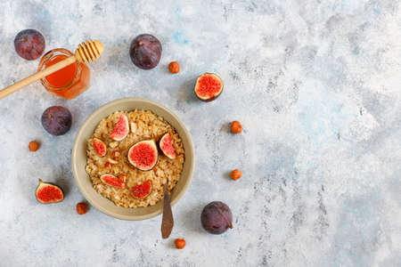 Oatmeal porridge with red figs and walnuts,honey in a bowl, above view on light backgroundの写真素材