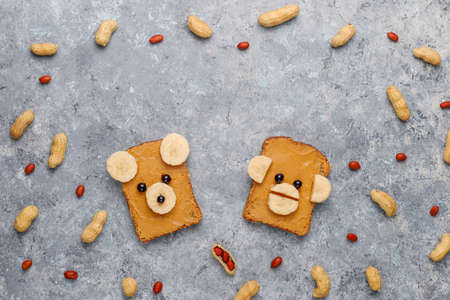 Funny bear and monkey face sandwich with peanut butter, banana and black currant,peanuts on grey concrete background,top viewの写真素材