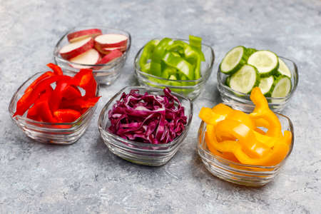 Cutting board with slices of colorful bell peppers on light background. Sliced sweet peppers in different colors, vegetable salad ingredient, cooking healthy food, top viewの写真素材