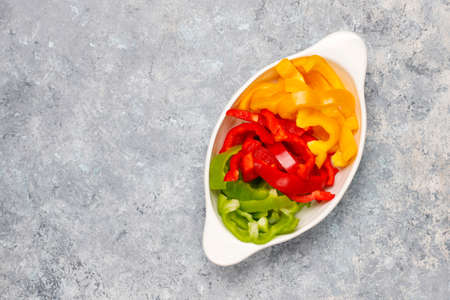 Cutting board with slices of colorful bell peppers on light background. Sliced sweet peppers in...