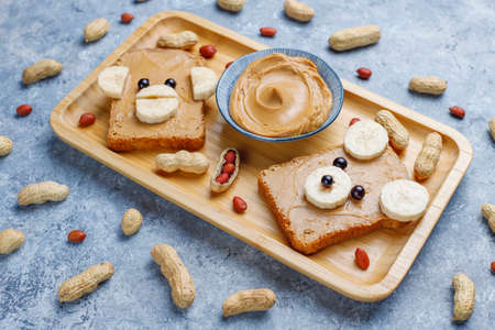 Funny bear and monkey face sandwich with peanut butter, banana and black currant,peanuts on grey concrete background,top viewの写真素材