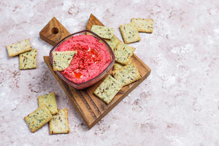 Beetroot hummus on cutting board with salty cookies on light background