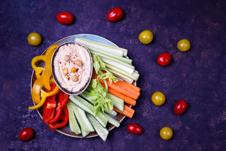 Plate of fresh organic vegetables salad with hummus on dark brown or concrete background, healthy flat layout food concept with fresh spring or summer vegetables, light dinnerの写真素材