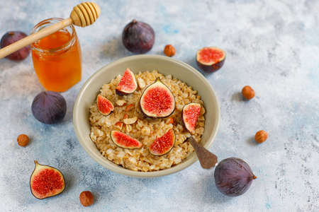 Oatmeal porridge with red figs and walnuts,honey in a bowl, above view on light backgroundの写真素材
