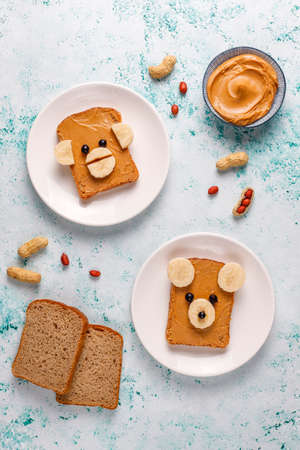Funny bear and monkey face sandwich with peanut butter, banana and black currant on light background,top viewの写真素材