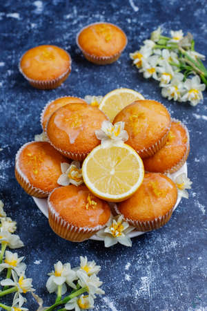 Delicious freshly baked homemade lemon muffins with lemons on a plate on dark background