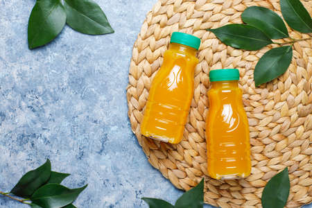 Plastic mini bottles of organic fresh orange juice with raw oranges and tangerines