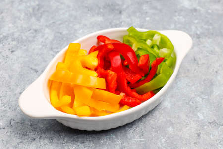 Cutting board with slices of colorful bell peppers on light background. Sliced sweet peppers in different colors, vegetable salad ingredient, cooking healthy food, top viewの写真素材