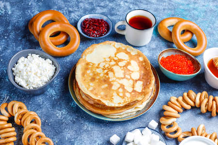 Shrovetide Maslenitsa festival meal. Russian pancake blini with raspberry jam, honey, fresh cream and red caviar,sugar cubes,cottage cheese,bubliks on dark backgroundの写真素材