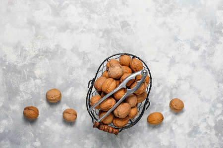 Whole walnuts in shell in food metal basket, walnut kernels. Top view on concrete background