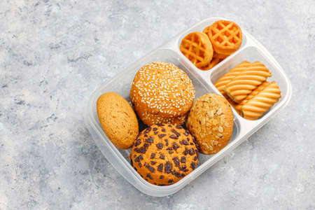 Unhealthy lunch box with cookies,waffles.muffins on concrete background