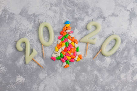 Candles in the shape of numbers 2020 as a symbol of the new year next to christmas shaped sparkle candies on a gray table. Top view, flat layの写真素材