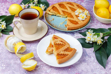 Delicious lemon pie slices with fresh lemons and a cup of tea on light background,top viewの写真素材