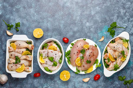 Raw chicken meat fillet, thigh, wings and legs with herbs ,spices,lemon and garlic on dark blue...