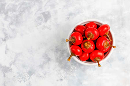 Pickled small round red hot cherry chili peppers on grey concrete backgroundの写真素材