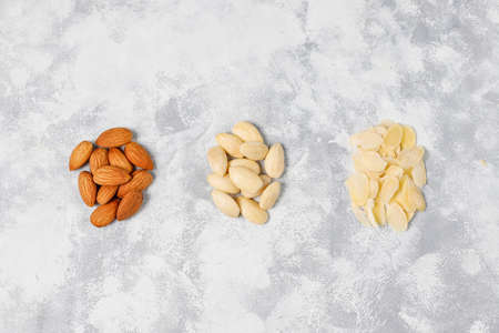 Peeled (blanched) and unblanched whole almonds on grey concrete background