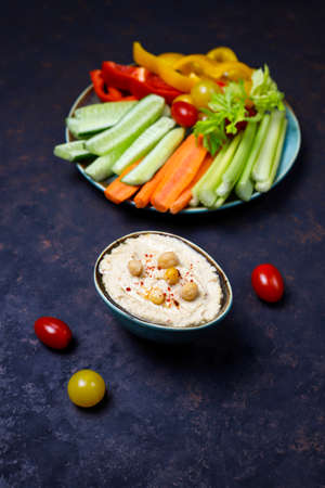 Plate of fresh organic vegetables salad with hummus on dark brown or concrete background, healthy flat layout food concept with fresh spring or summer vegetables, light dinnerの写真素材