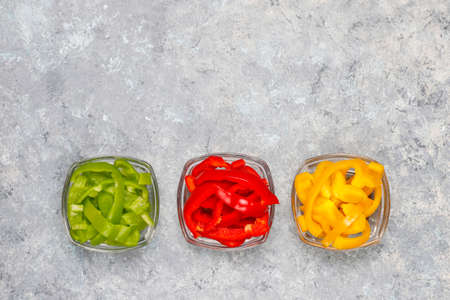Cutting board with slices of colorful bell peppers on light background. Sliced sweet peppers in different colors, vegetable salad ingredient, cooking healthy food, top viewの写真素材