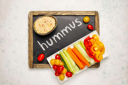 Plate of fresh organic vegetables salad with hummus on light concrete background, healthy flat...